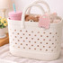 A basket with a white design featuring holes, holding a pink drink bottle, a teddy bear, and a soft toy.