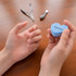 A heart-shaped blue container holding nail files, held by hands, with manicure tools nearby on a wooden surface.