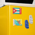 Fridge magnets in various designs, including a flag, a drum, and a pair of white and blue slides on a yellow fridge.