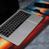 A metallic laptop sits on a vibrant full-colour print rubber desk mat featuring abstract designs in red, orange, and blue.