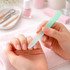 A gradient glass nail file with a mint green handle rests against a hand with neatly manicured nails on a pink towel.