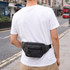 A grey canvas waist bag worn at the back of a person, standing on a street.