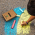 A set of jumbo sidewalk chalk pieces in various colours, with a cardboard box featuring a logo on the ground.