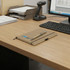 A kraft notebook with a pen rests on a wooden desk beside a computer and document organiser.
