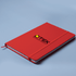 A red A5 notebook with an elastic band and a branding logo on the cover.