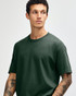 A heavyweight cotton unisex t-shirt in dark green, worn by a model with curly hair. Features a simple, classic design.