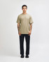 A unisex heavyweight cotton t-shirt in olive green, paired with light blue cargo jeans. The model has curly hair.