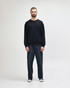 A black crewneck sweatshirt is worn by a person paired with blue jeans and white sneakers, featuring a logo.
