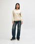 A cream-coloured crewneck sweatshirt is worn by a model paired with light blue jeans and white sneakers.