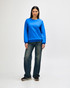A woman wearing a blue Gildan Heavy Blend crewneck sweatshirt paired with blue jeans and white sneakers.