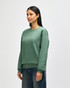 A green crewneck sweatshirt on a model, featuring long sleeves and a relaxed fit. The product has a logo.