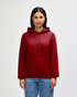A red hooded sweatshirt with a front pocket and drawstring hood. The model is posed against a plain backdrop.