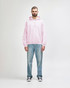 A man stands wearing a pink hooded sweatshirt and black jeans, with his hands in the pockets of the sweatshirt.