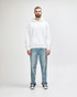 A white hooded sweatshirt worn by a young man, paired with black jeans and sneakers. The sweatshirt features a logo.