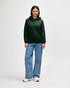 A woman wearing a green hooded sweatshirt with a kangaroo pocket, paired with blue jeans and white sneakers.