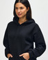 A black Gildan Heavy Blend adult hooded sweatshirt, featuring a drawstring hood and a model adjusting the neckline.