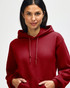 A red hooded sweatshirt is worn by a young man adjusting the hood near his face. The sweatshirt features a logo.
