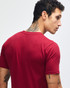 A model wears a maroon unisex fine jersey short sleeve T-shirt paired with blue jeans. The T-shirt features a logo.