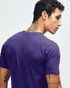 A purple short sleeve t-shirt featuring a logo, viewed from the back on a model.