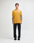 A unisex short sleeve t-shirt in mustard yellow, worn with black cargo pants, featuring a logo.