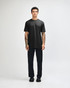 A black unisex short sleeve t-shirt worn with light blue baggy jeans and black sneakers. The model poses against a plain background.