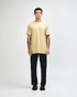 A unisex short sleeve T-shirt in a light khaki colour, worn with black cargo pants, features a logo.