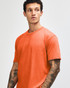 An orange unisex short sleeve T-shirt is displayed on a model with a neutral background. The shirt has a simple design and consists of soft fabric.