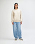 A unisex crewneck sweatshirt in beige worn with light blue jeans and black sneakers, featuring a logo.