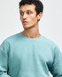 A unisex crewneck sweatshirt in green, featuring a relaxed fit and a simple design. It has a logo on it.