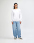 A unisex crewneck sweatshirt in white, paired with light blue baggy jeans, worn by a model. Features a branding logo.