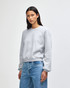 A grey women's crewneck sweatshirt with a relaxed fit and branding, styled with casual jeans.