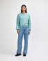 A woman wearing a teal crewneck sweatshirt with a relaxed fit, paired with loose light blue jeans.