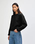 A women's black crewneck sweatshirt displayed on a model, featuring long sleeves and a relaxed fit.