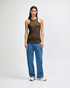 A woman wearing an olive green racerneck tank top and loose blue cargo jeans, standing with a relaxed pose.