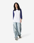 A unisex raglan T-shirt featuring white fabric with navy blue sleeves, worn with casual baggy pants.