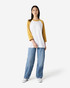 A unisex raglan t-shirt with white body and mustard yellow sleeves, paired with loose blue jeans.