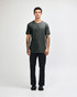 A man stands wearing a dark grey unisex Henley T-shirt paired with light blue jeans and black sneakers.
