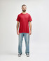 A red Gildan Heavy Cotton Adult T-Shirt worn by a model, paired with black jeans and sneakers. The shirt has a logo.
