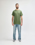 A green Gildan Heavy Cotton Adult T-Shirt, worn by a model paired with black jeans and sneakers, standing against a white background.