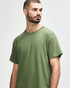 A man models a Gildan Heavy Cotton Adult T-Shirt in olive green, featuring a simple design and a logo.