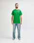 A green Gildan Heavy Cotton adult t-shirt displayed on a mannequin styled with black jeans and sneakers.