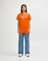 An orange Gildan Heavy Cotton adult T-shirt worn by a standing male model, paired with black jeans and sneakers.