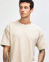 A light beige super heavyweight T-shirt on a model, featuring a relaxed fit and short sleeves. It has a logo.