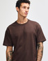 A brown super heavyweight t-shirt on a model with tattoos, featuring a plain design and a logo on the garment.