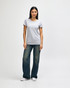 A grey ladies' T-shirt is worn by a model, paired with blue jeans and white sneakers. The shirt features a logo.