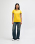 A woman wearing a yellow Gildan Heavy Cotton ladies' t-shirt paired with blue jeans and white sneakers.