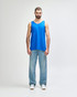 A blue tank top displayed on a model wearing black pants and sneakers, featuring a logo.