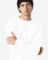 A white long sleeve T-shirt on a model with a neutral background, featuring a logo on the sleeve.