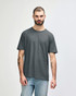 A man wearing a dark grey Gildan Softstyle adult T-shirt, paired with light blue jeans. The t-shirt has a logo.