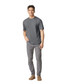 A man stands wearing a grey Gildan Softstyle adult T-shirt paired with light grey jeans and casual footwear.